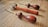 Three leatherworking tools with wooden handles rest on a wooden surface. The tools have curved metal tips and brass accents near the handles.