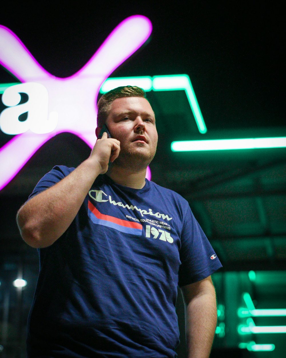 a man talking on a cell phone in front of a neon sign