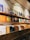 A collection of vinyl records displayed on wooden shelves, with album covers depicting various art styles and themes. The upper shelf holds a row of colorful album covers, while the lower shelf features records in plain sleeves organized in sections labeled with different music genres such as Deep House and Techno. Above the albums, a wavy line is painted on the wall as decorative art.