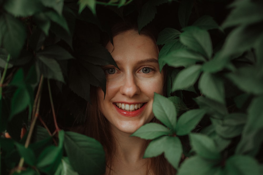 a woman is smiling through the leaves of a tree