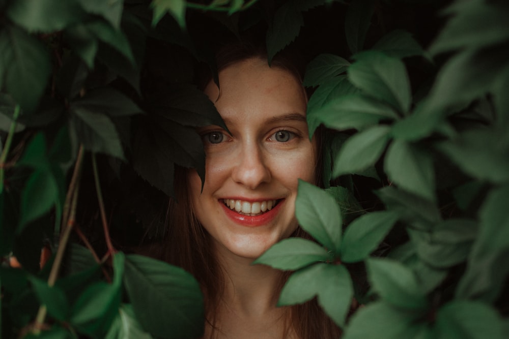 Une femme sourit à travers les feuilles d’un arbre