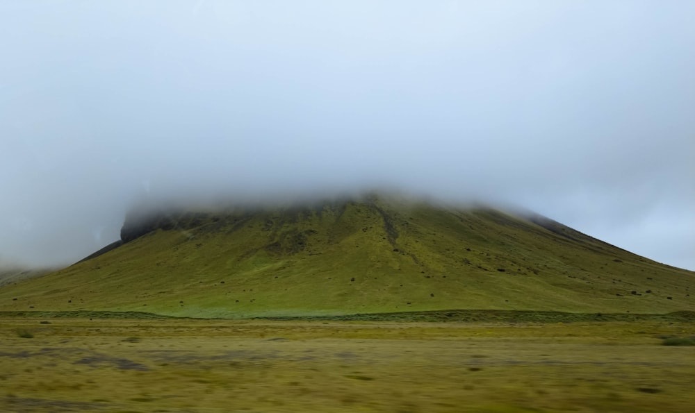 a large green mountain covered in fog and clouds