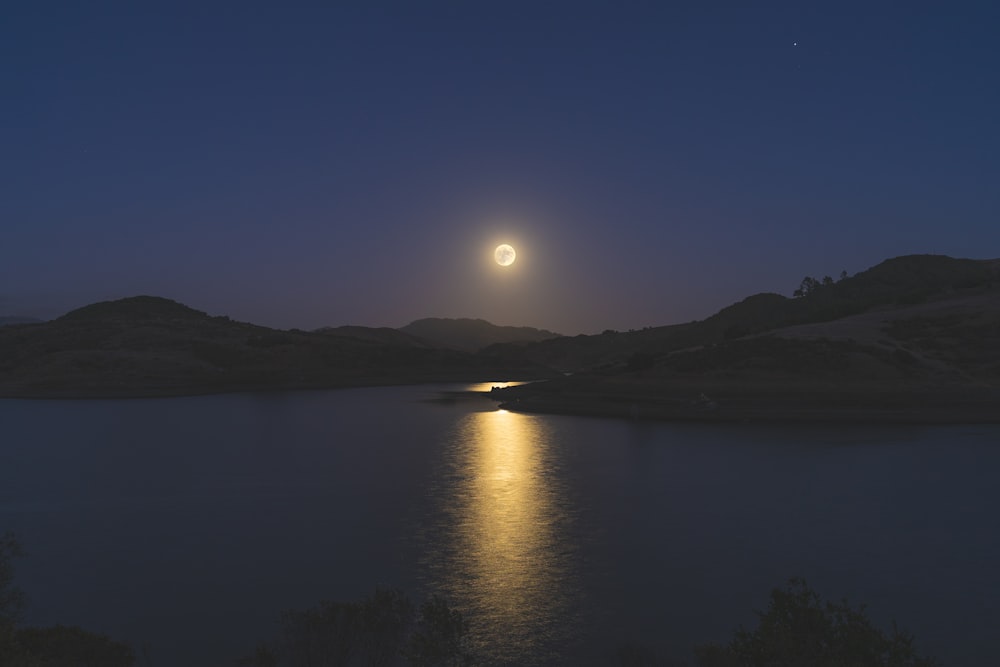 a full moon rising over a lake with mountains in the background