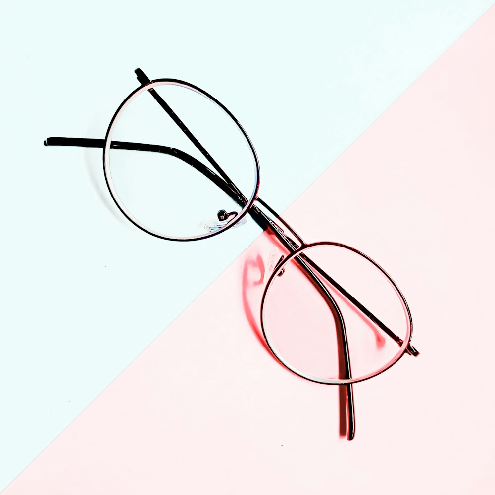 Un par de gafas sentadas sobre un fondo rosa y blanco