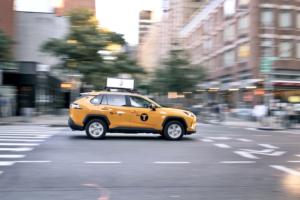 a yellow car driving down a street next to tall buildings