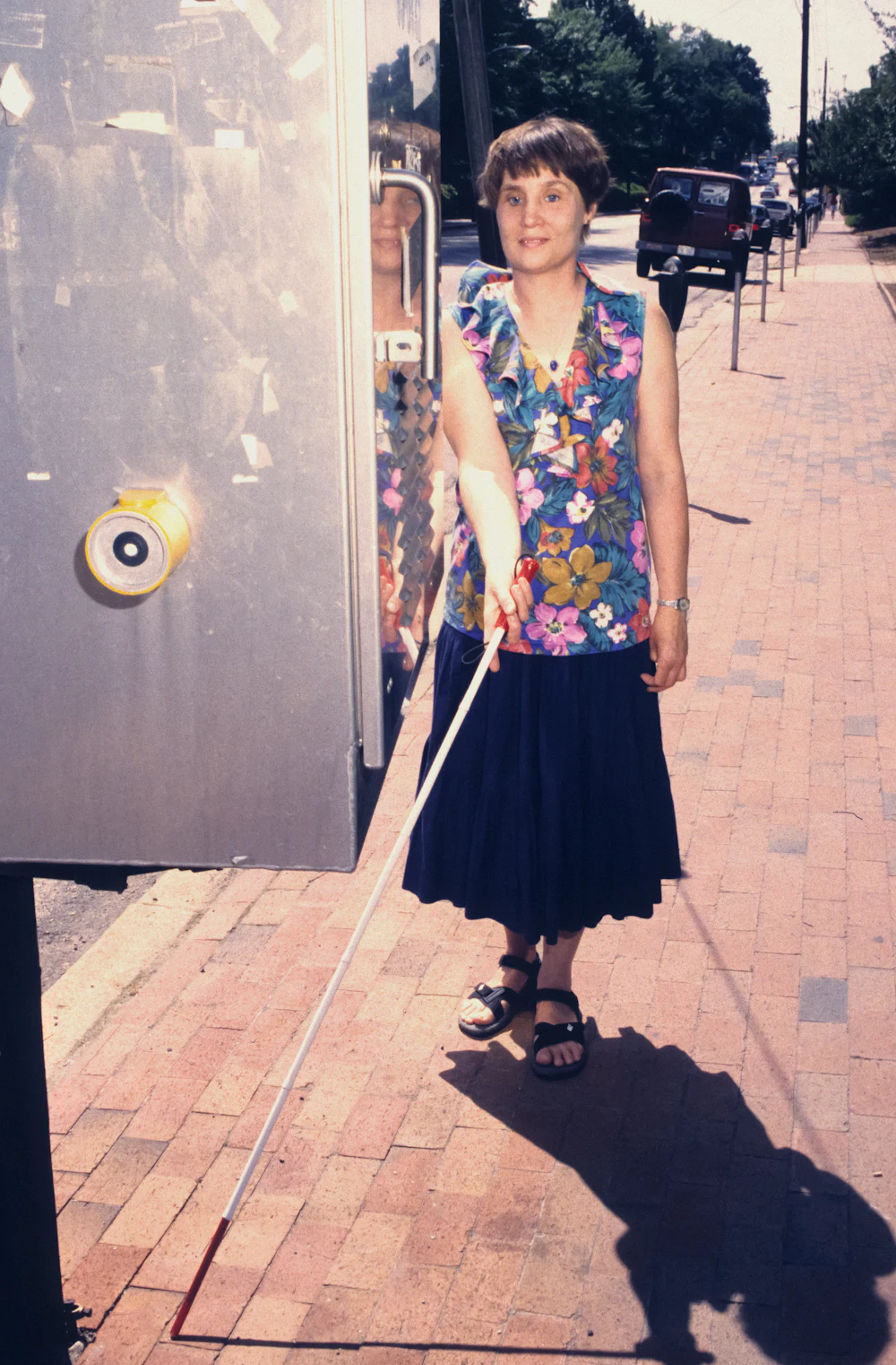 A woman with a white cane waiting beside a bus