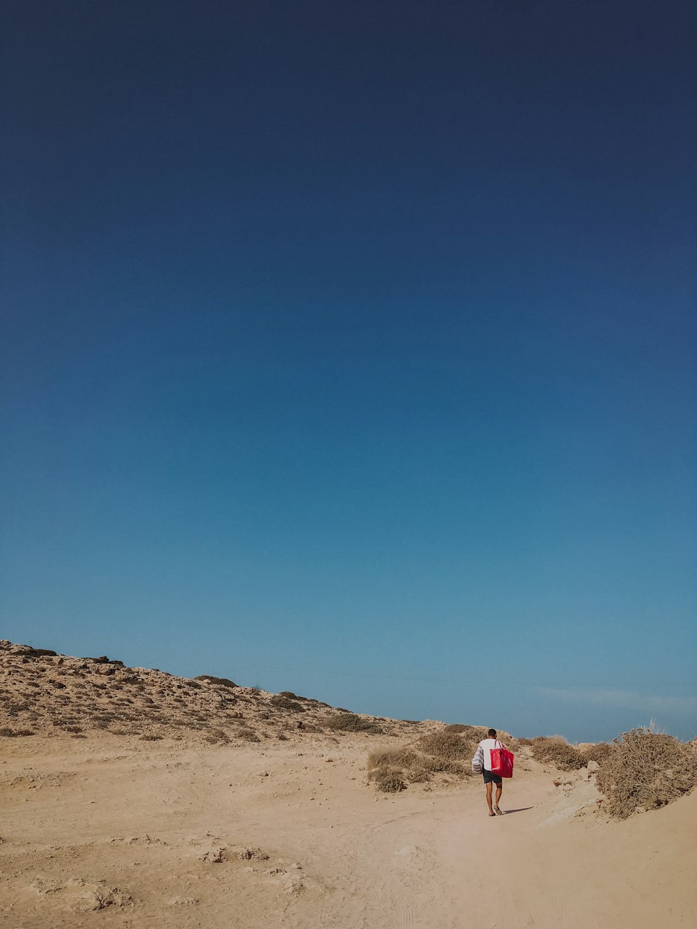 a person walking on a sandy beach under a blue sky