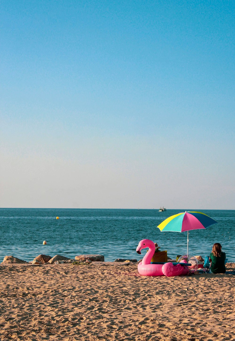 two people sitting on a beach with an inflatable flamingo