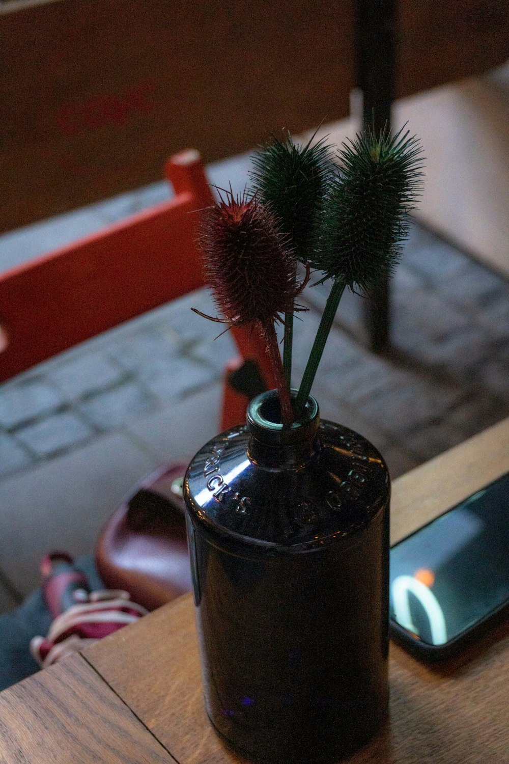 a table with a cell phone and a vase with flowers in it