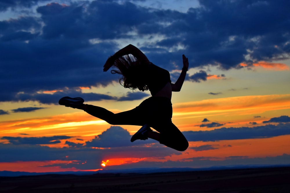 uma mulher que salta no ar ao pôr do sol