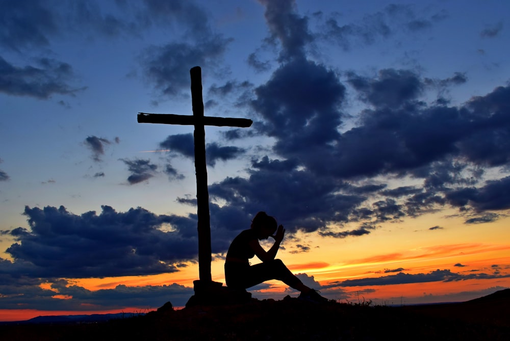 une personne assise sur une colline avec une croix en arrière-plan