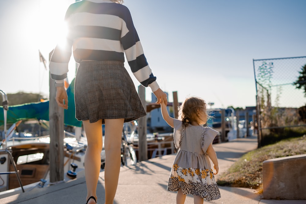 a woman walking down a sidewalk holding the hand of a little girl