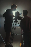 two men standing in front of a camera on a tripod