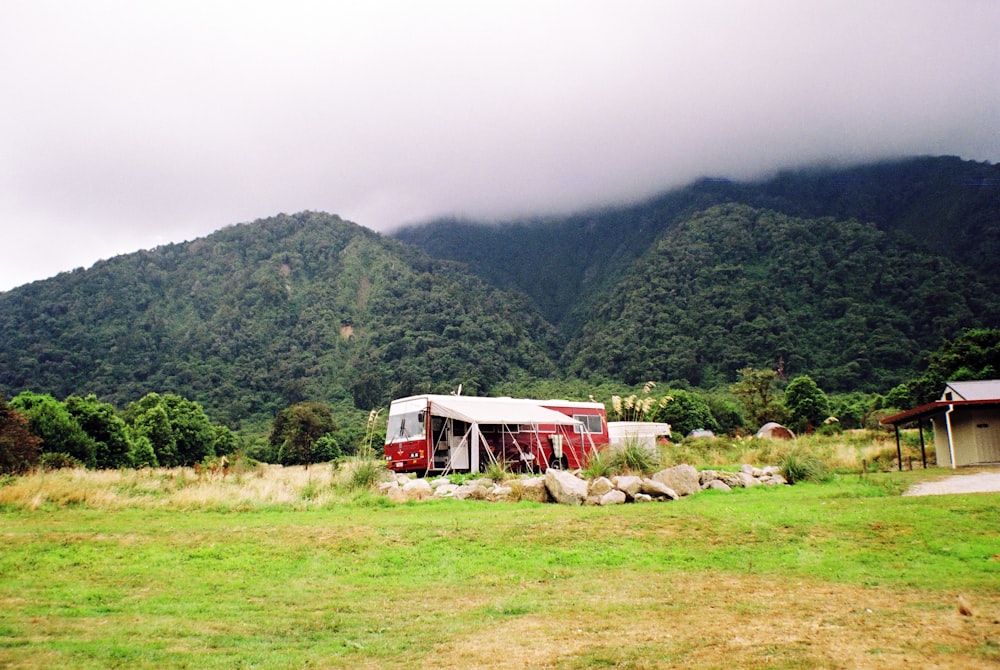 a red and white bus parked on top of a lush green field