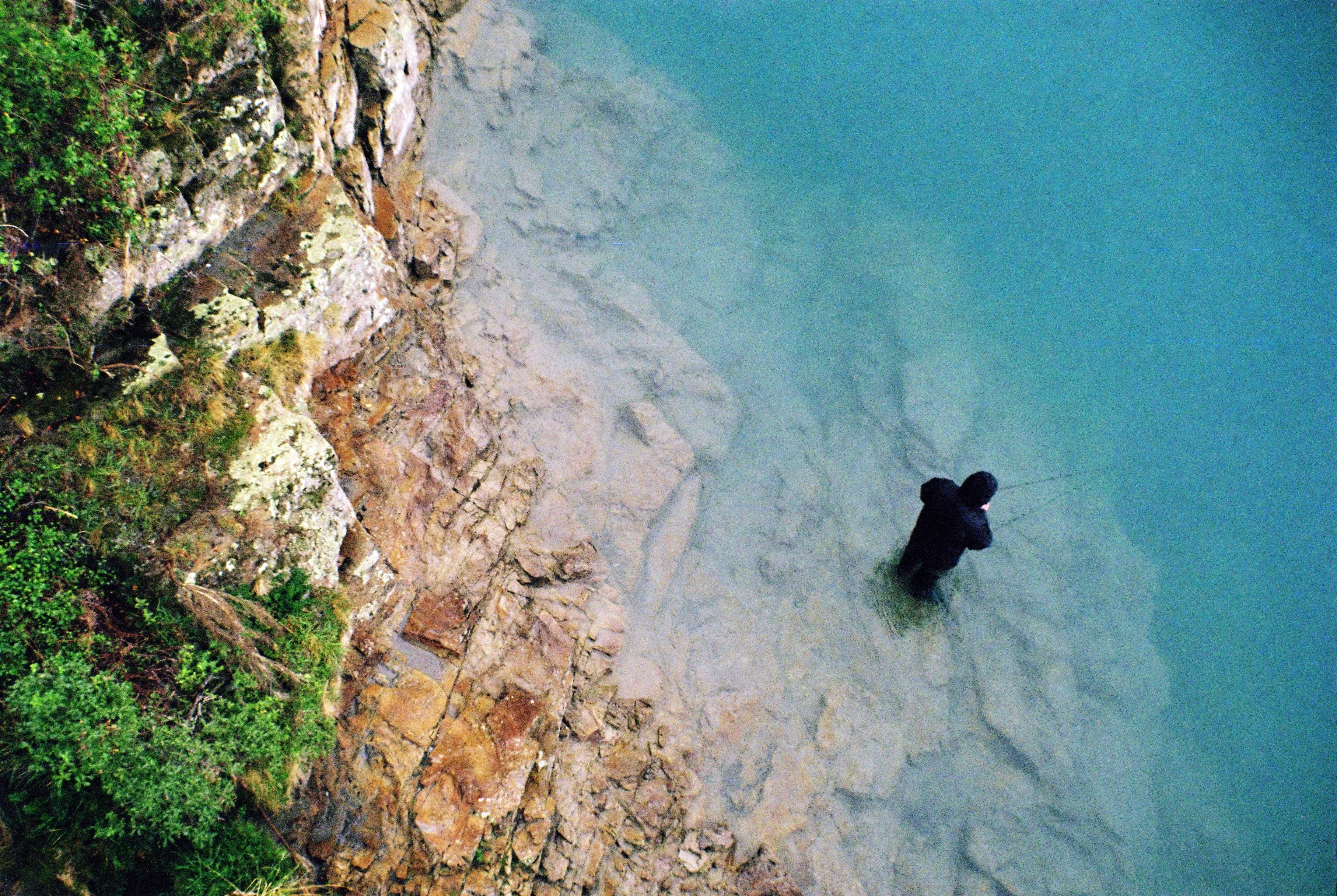 a black dog standing in the water next to a cliff