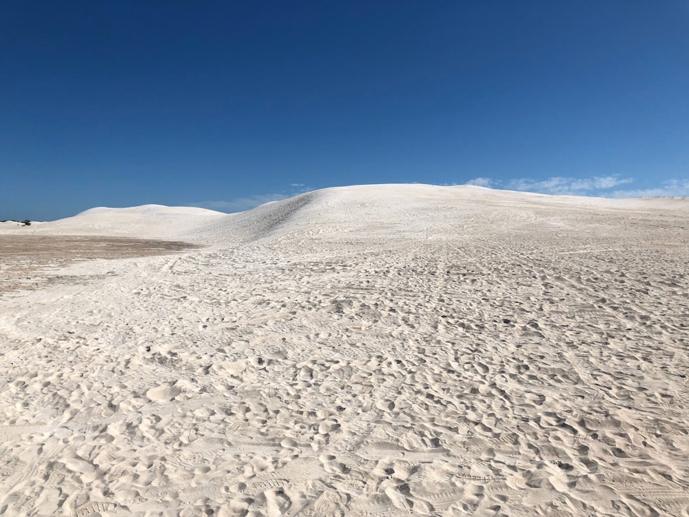 a sandy beach with footprints on it under a blue sky