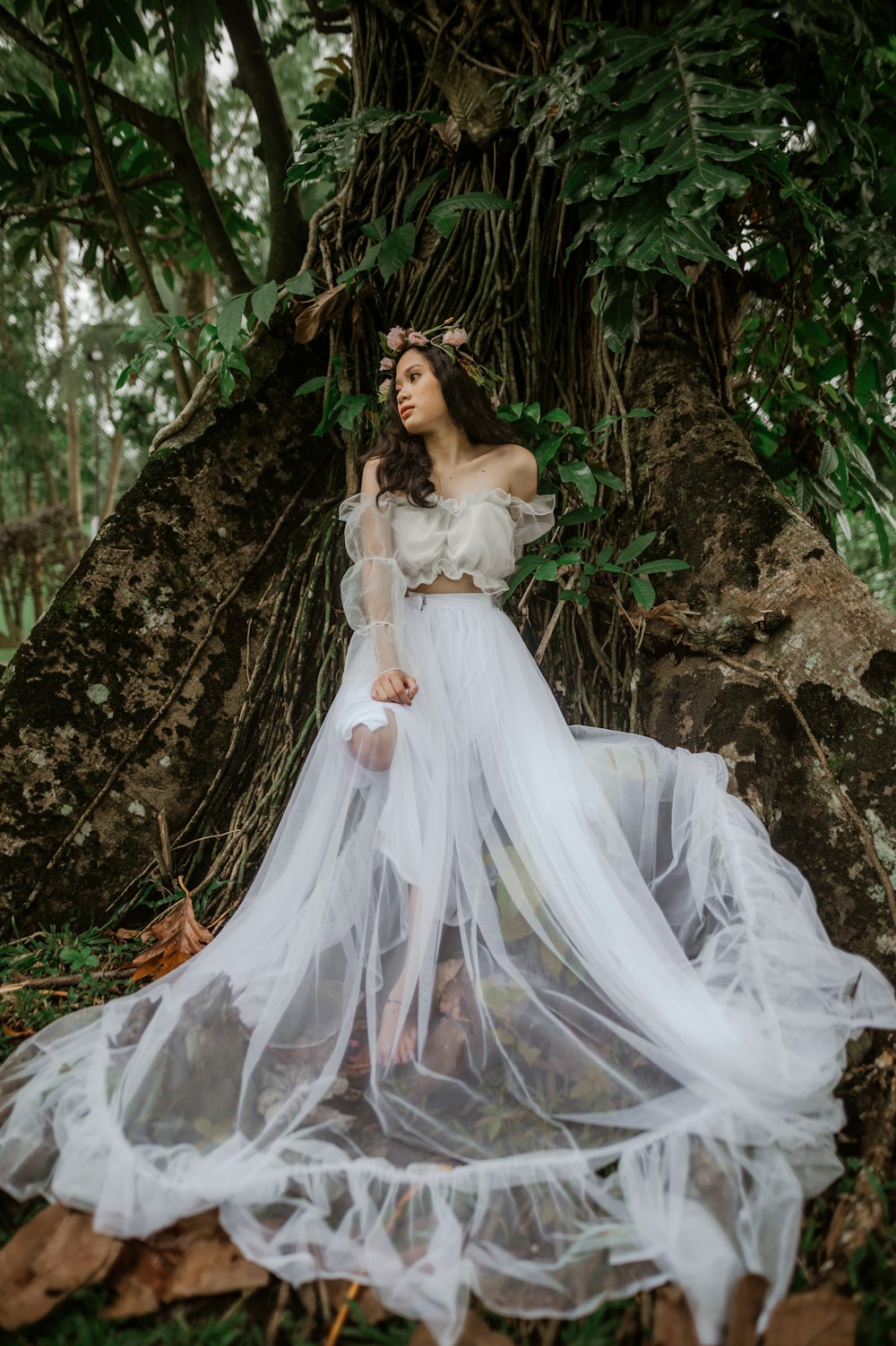 a woman in a white dress standing in front of a tree