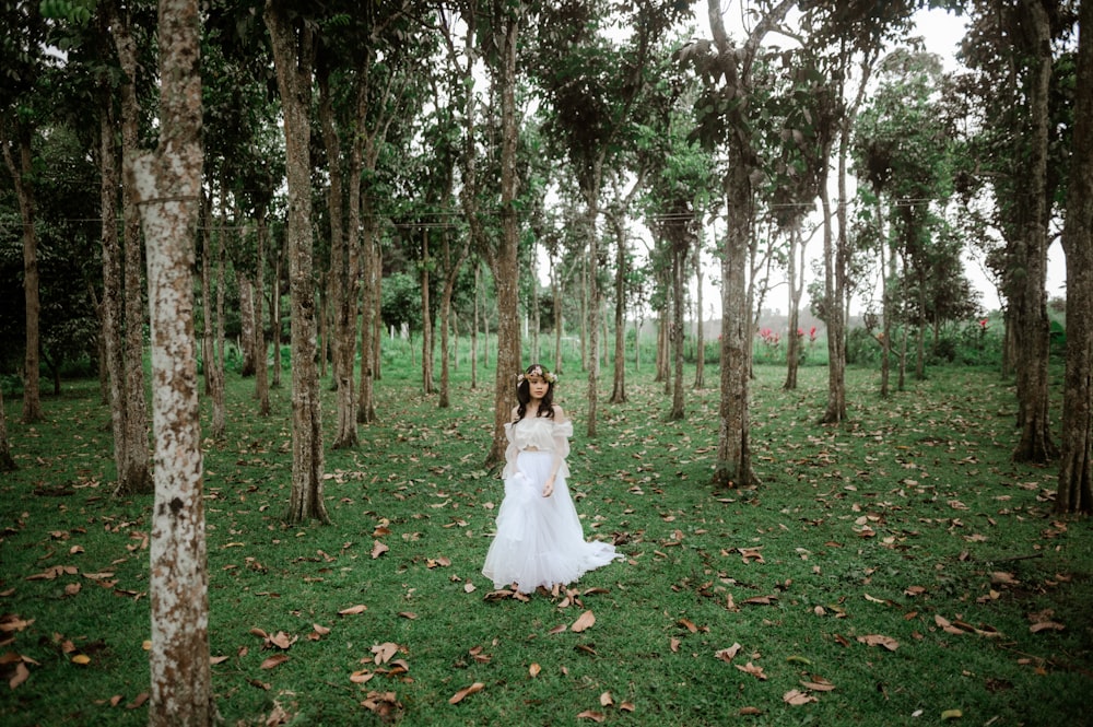 a woman in a white dress standing in a forest