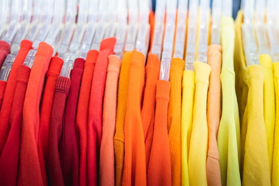 A collection of brightly colored shirts organized on hangers. The shirts range from shades of red on the left to yellows on the right.