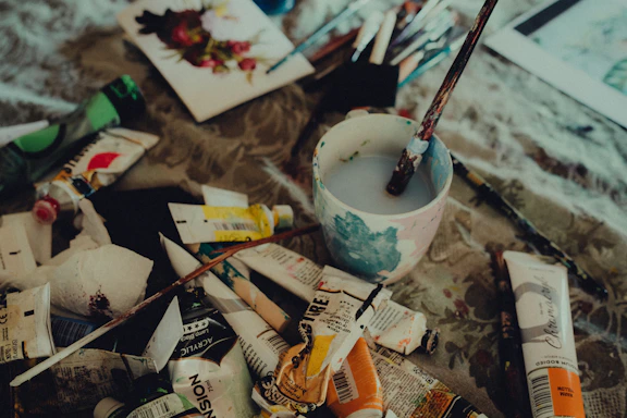 A cozy artist's workspace with watercolor paints, ink pens, and a half-finished portrait on textured paper.