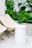 A minimalist outdoor setup featuring two beige folding chairs and a cylindrical white stool on a light tiled floor. Lush green tropical plants in the background add a fresh, natural element to the scene.
