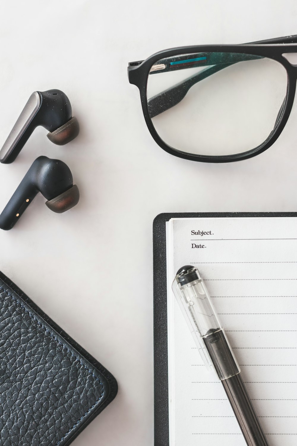 a notepad, pen, glasses, and a pair of headphones on a