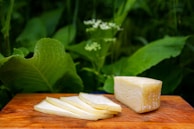 A detailed shot of a knife cutting into a creamy, soft cheese on a wooden board.