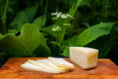 Handmade cheese blocks wrapped in natural leaves on a wooden board.