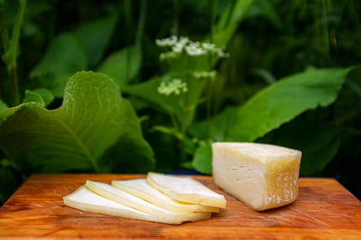 A block of fresh white paneer on a rustic wooden board with a knife beside it.