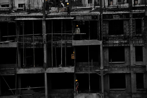 A sturdy construction site with workers in yellow helmets and navy blue uniforms coordinating a modern building framework.