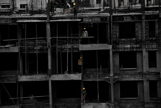 A sturdy modern building under construction with workers in yellow helmets against a deep navy sky.