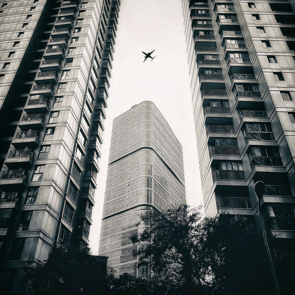 a black and white photo of a plane flying in the sky between two tall buildings