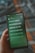 A smartphone displaying song lyrics in Chinese on its screen. The phone is being held in a person's hand, and the background is blurred, featuring soft colors and patterns.