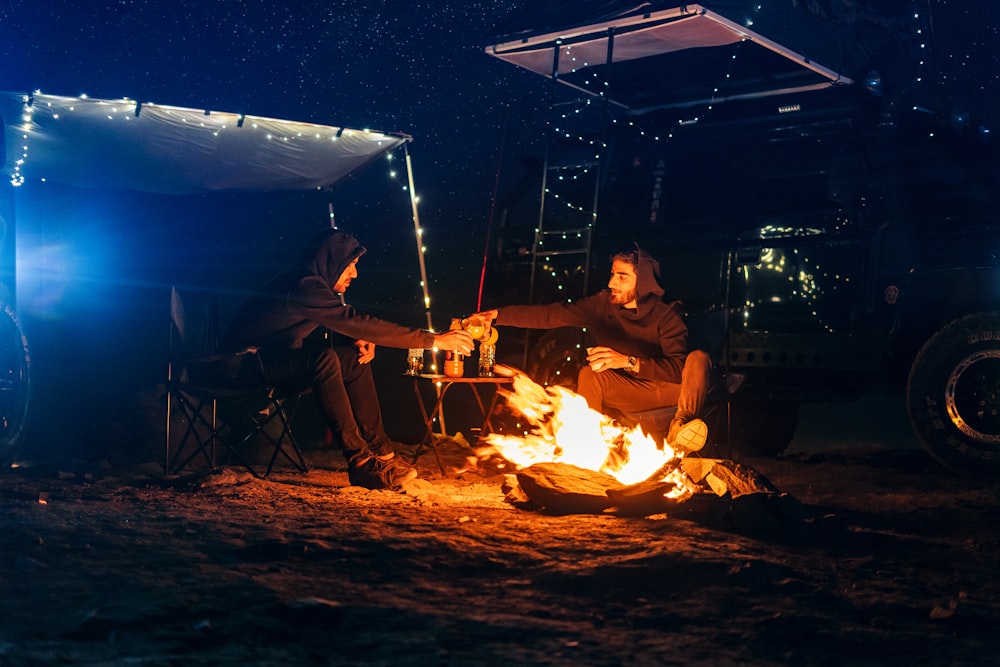 two people sitting around a campfire at night