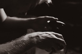 A close-up black and white photograph capturing the hands of a person holding a gaming controller. The focus is on the intricate details of the hands, highlighting the texture and veins. The background is softly blurred, drawing attention to the subject's concentration.