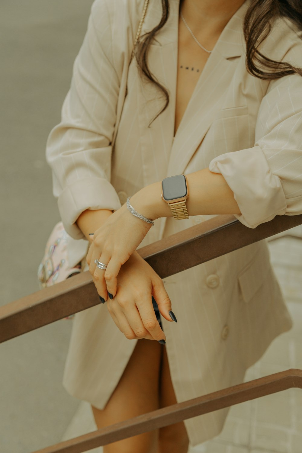 a woman in a beige suit and bracelets holding onto a railing