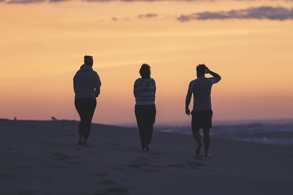 three people walking on a beach at sunset