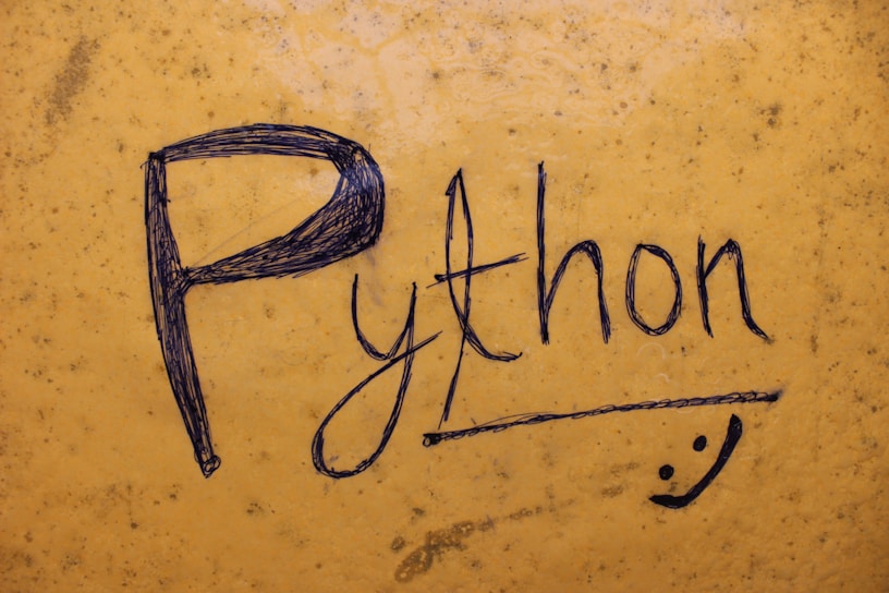 The word 'Python' is handwritten in black ink on a textured yellow surface. The letters are bold and artistic, with a small doodle of a smiley face underneath.