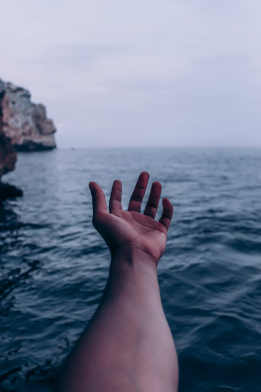 a person's hand reaching out to the ocean