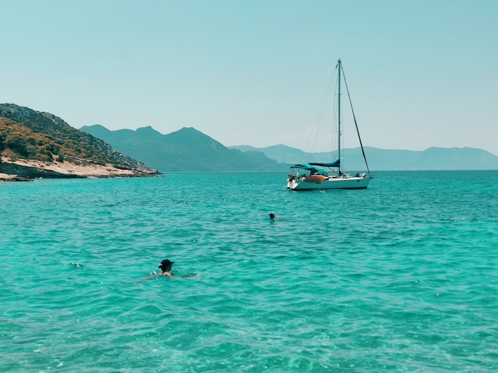 a person swimming in the ocean with a sailboat in the background