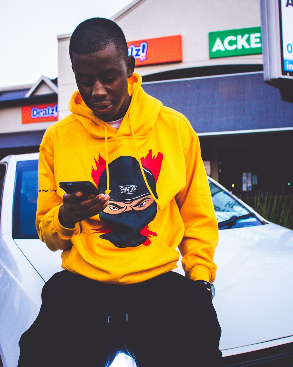 a man in a yellow hoodie looking at his cell phone
