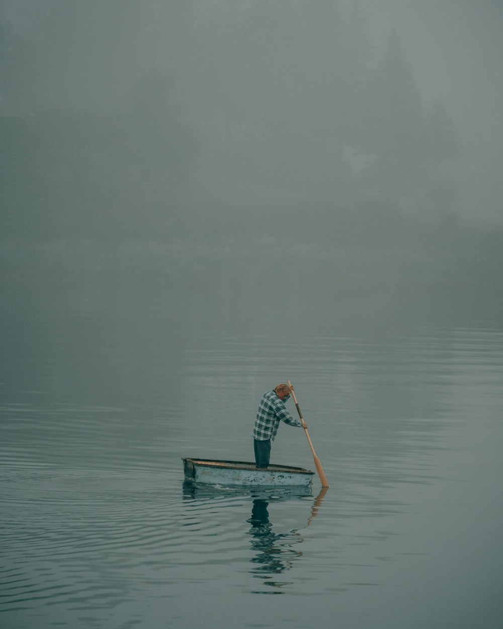 a man rowing a boat on a foggy lake