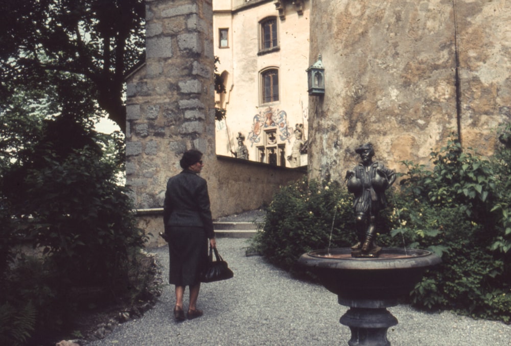 a woman walking past a statue in a garden