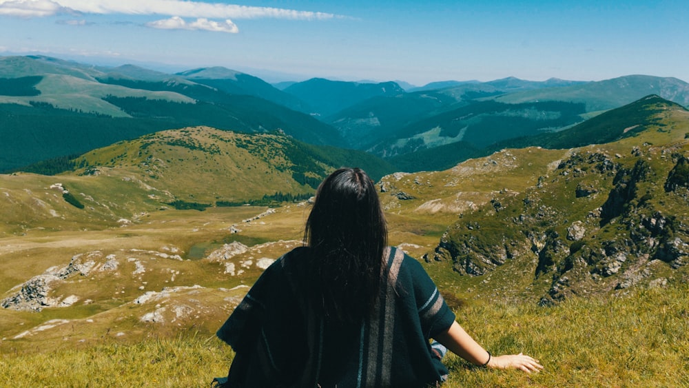 a woman sitting on top of a lush green hillside