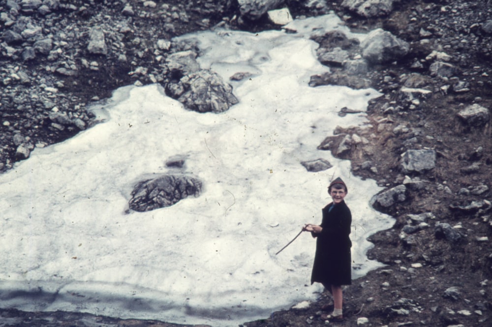 a woman in a black dress standing in front of a snow covered mountain