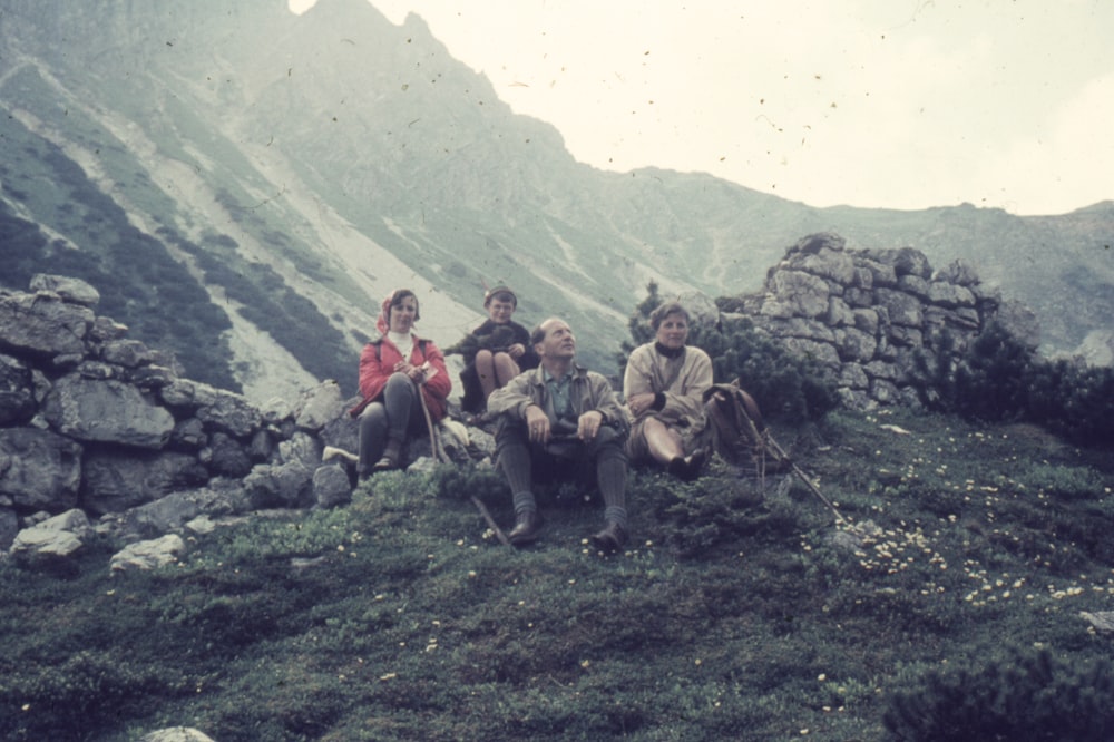 a group of people sitting on top of a grass covered hillside