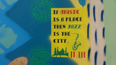A colorful poster with the text 'If music is a place, then jazz is the city' in various fonts. The poster has illustrations of a saxophone, a city skyline, and decorative patterns in the background. The background is a bright mix of blue, green, and yellow with some abstract shapes.