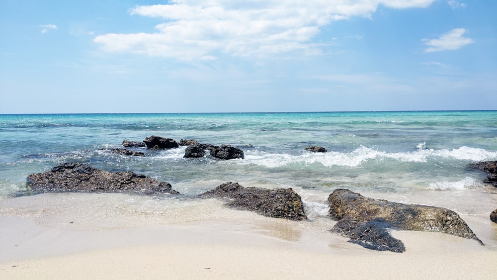 a beach with rocks and water on a sunny day