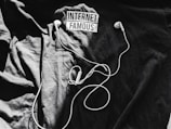 A black t-shirt is laid out with the words 'Internet Famous' printed on it. White earbuds with tangled cords rest on top of the shirt, creating a contrast against the dark background.