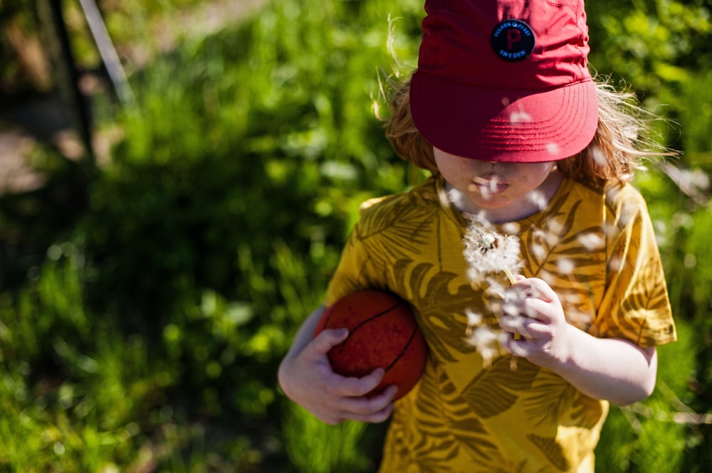 a little girl in a red hat holding a red ball